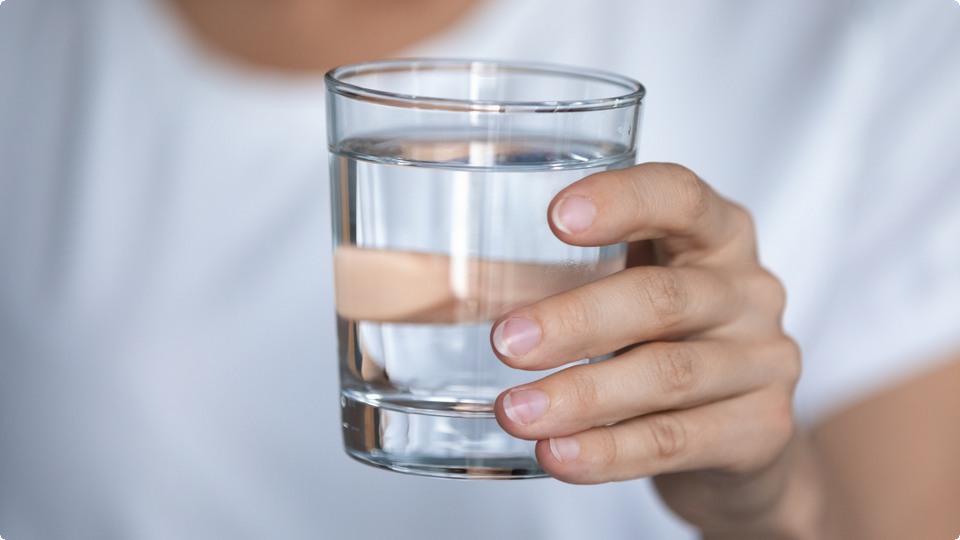 En hand håller i ett glas med vatten.