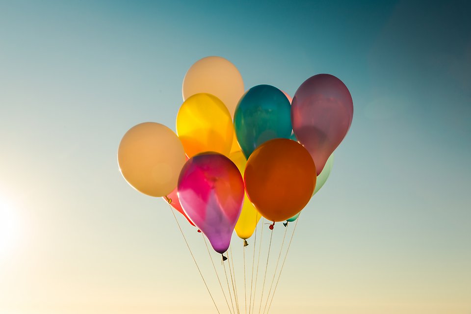 Knippe med färgglada ballonger mot blå himmel.