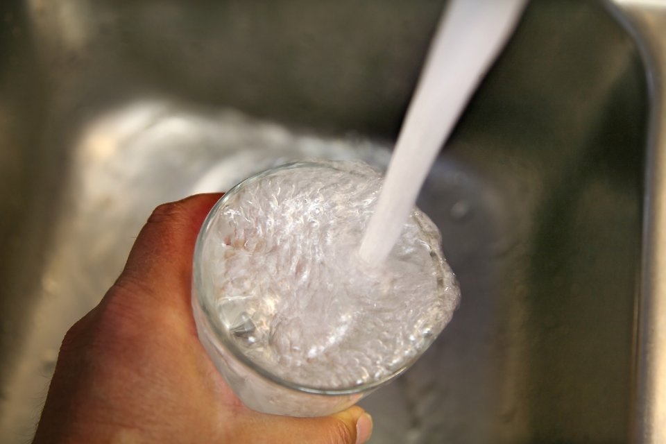 Hand som håller i glas som fylls på med vatten från kran.